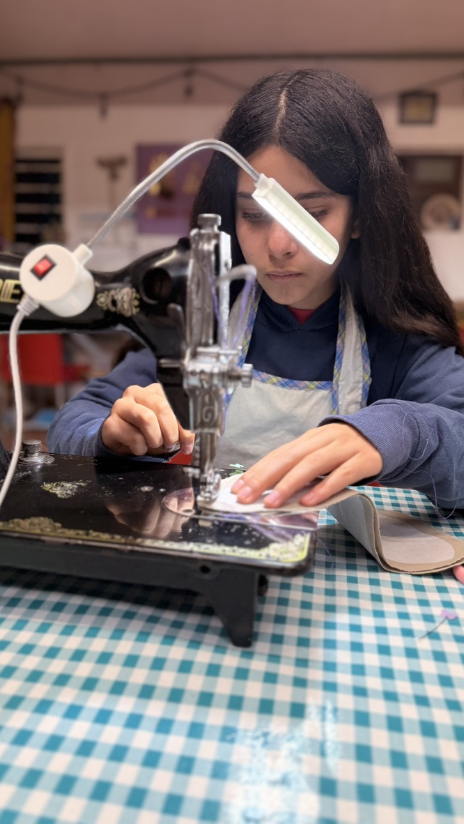 Alumna de Diseñadoras cosiendo en máquina vintage con lámpara en el taller de Ámate
