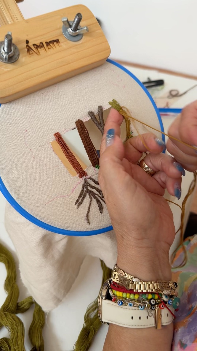 Manos bordando sobre bastidor con el nombre Ámate grabado en madera