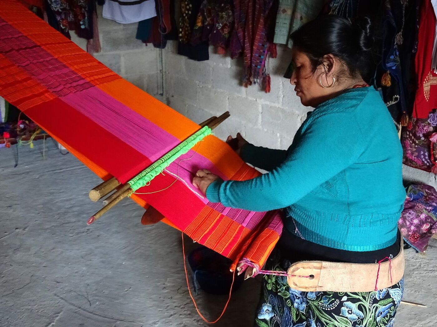 Tejedora tzotzil de Zinacantán trabajando en un telar de cintura con hilos naranjas, rosas y rojos